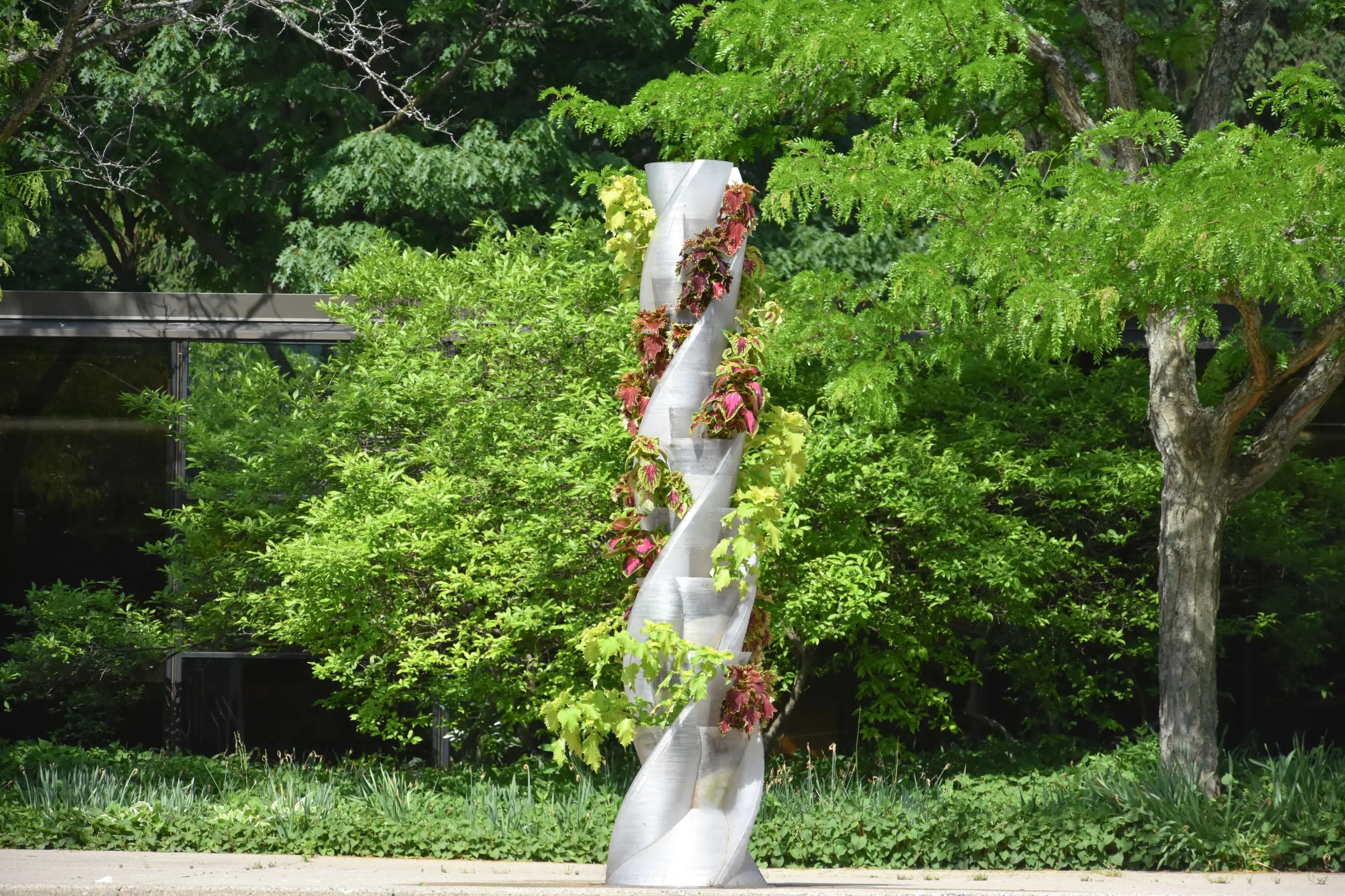 The printed PETG tower planted with coleus and vines, standing in a garden.