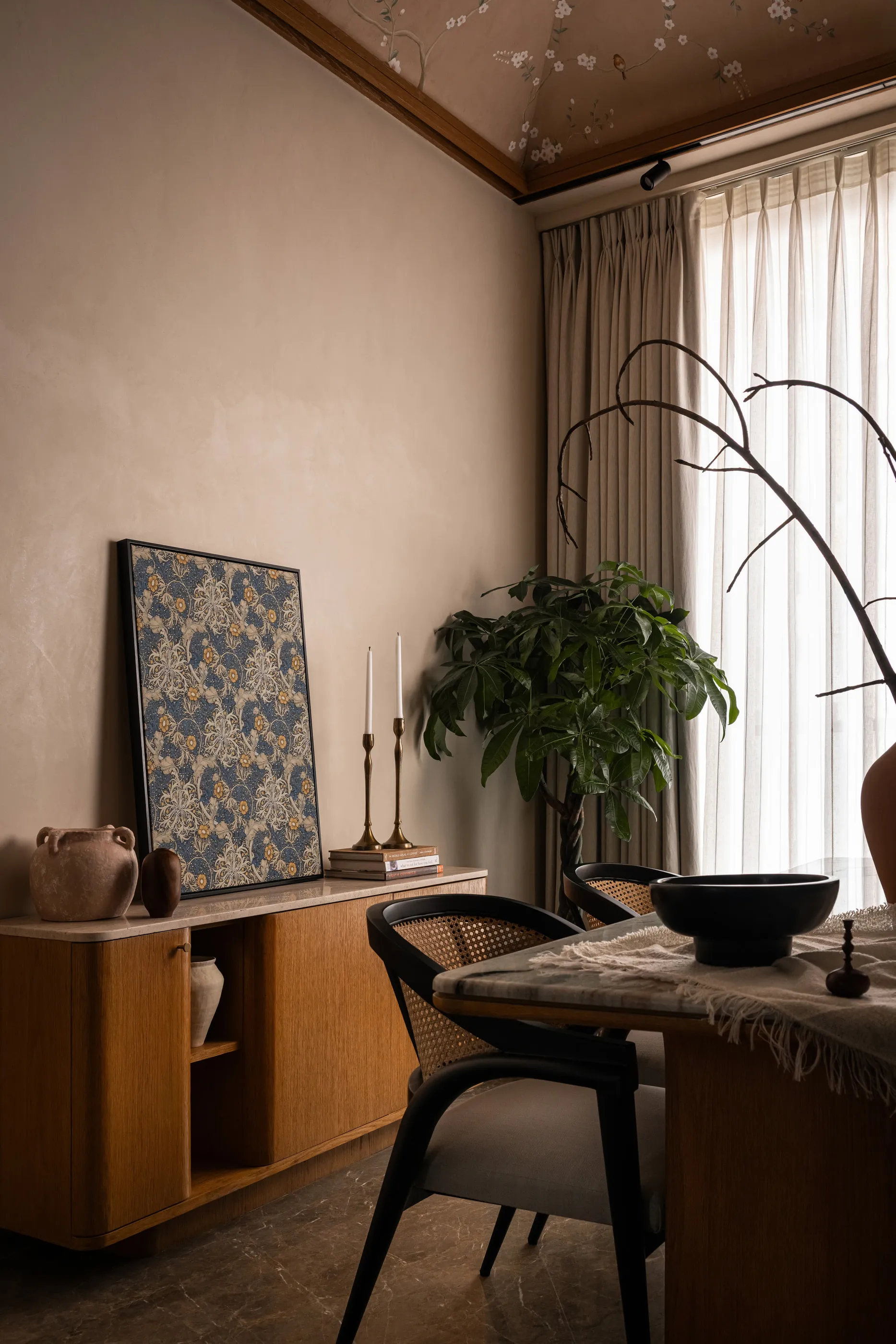 Oak sideboard with a framed floral print, candlesticks and a cane dining chair beside a tall window