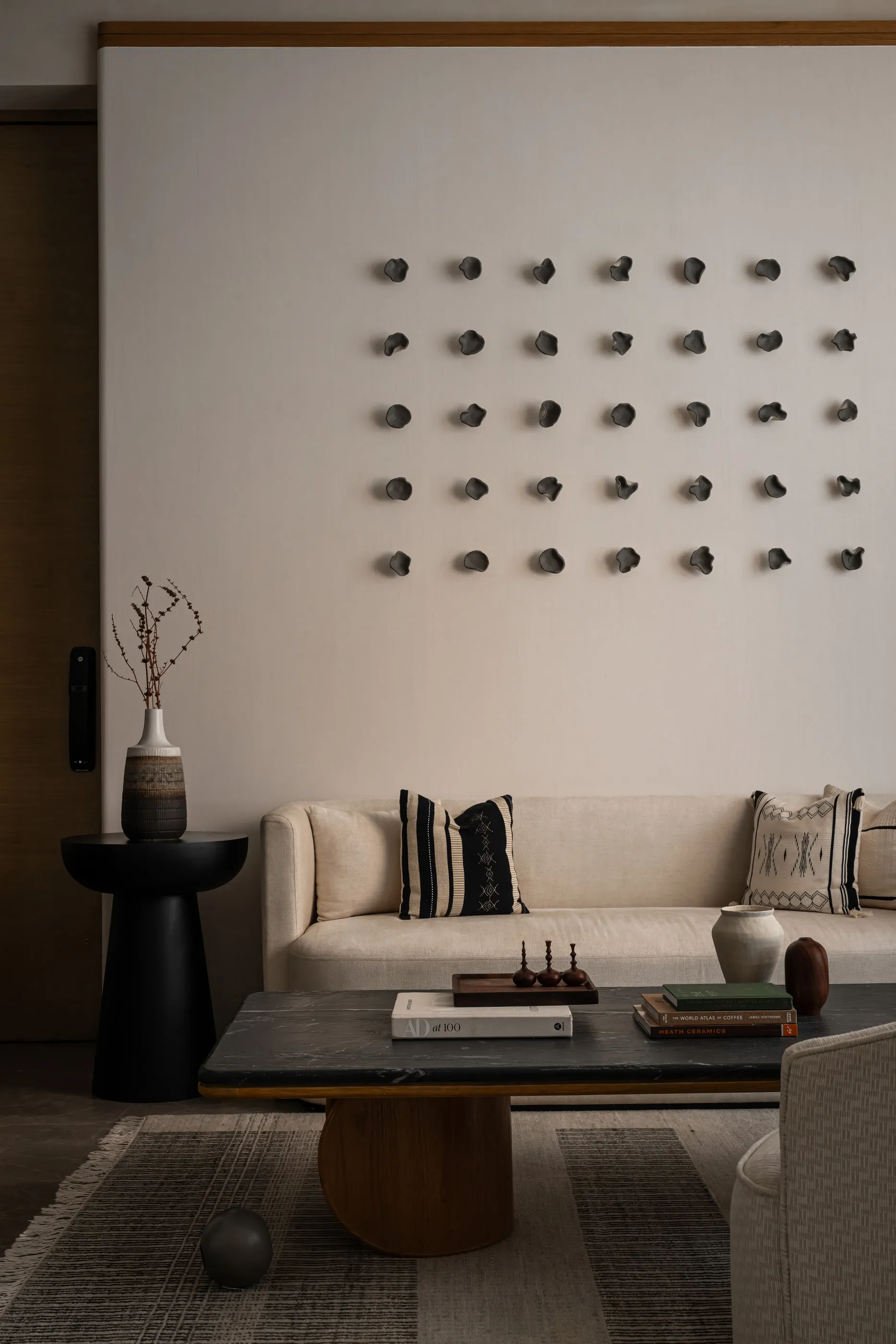 Living room sofa under a wall of small clay discs, with a black side table and low coffee table