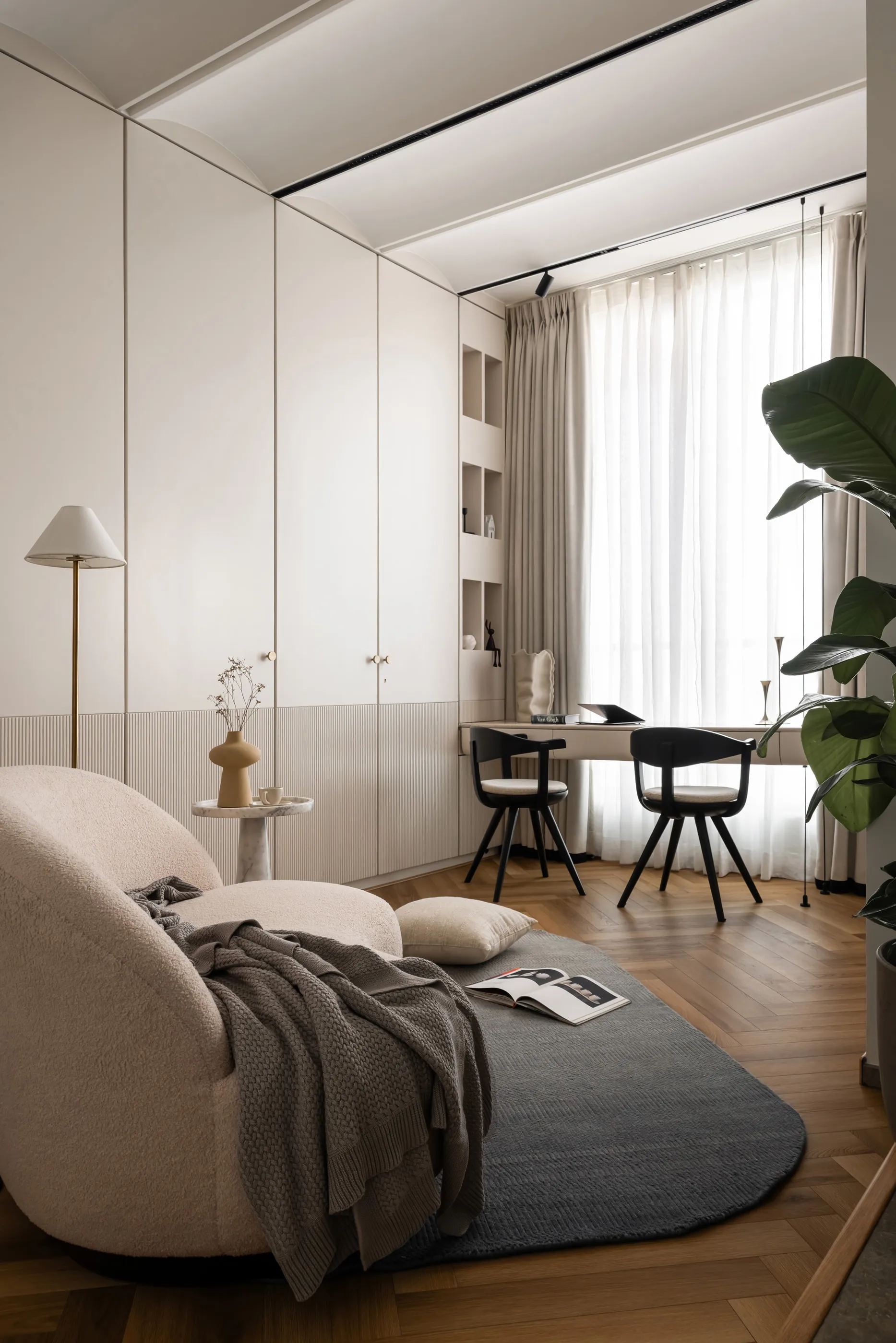 Study corner with a boucle lounge chair, arched built-in wardrobes and a desk by a sheer-curtained window